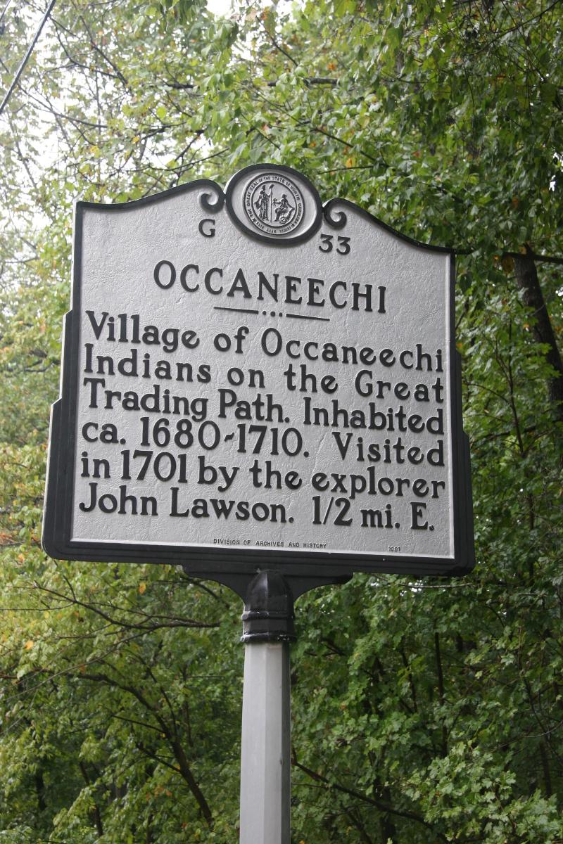 Large metallic marker that reads: &quot;OCCANEECHI, Village of Occaneechi Indians on the Great Trading Path. Inhabited ca. 1680-1710. Visited in 1701 by the explorer John Lawson. 1/2 mi. E.&quot;