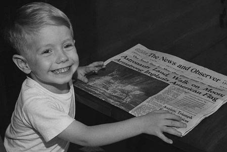 PHOTO OF DWAYNE CLARK, AGE 3 1/2 YEARS OLD, SON OF MR. & MRS. CHARLES CLARK, HOLDING A COPY OF THE &quot;NEWS & OBSERVER,&quot; JULY 21, 1969, ANNOUNCING THE FIRST MOON LANDING